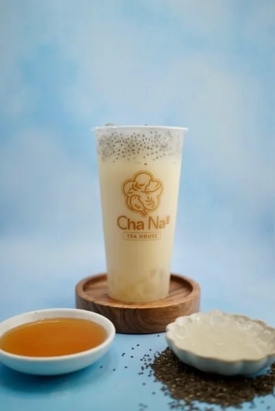 A creamy beverage with chia seeds, served in a branded cup alongside honey and a small bowl of jelly.