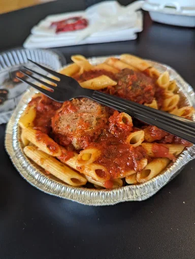 A serving of pasta with marinara sauce and meatballs, accompanied by a plastic fork.