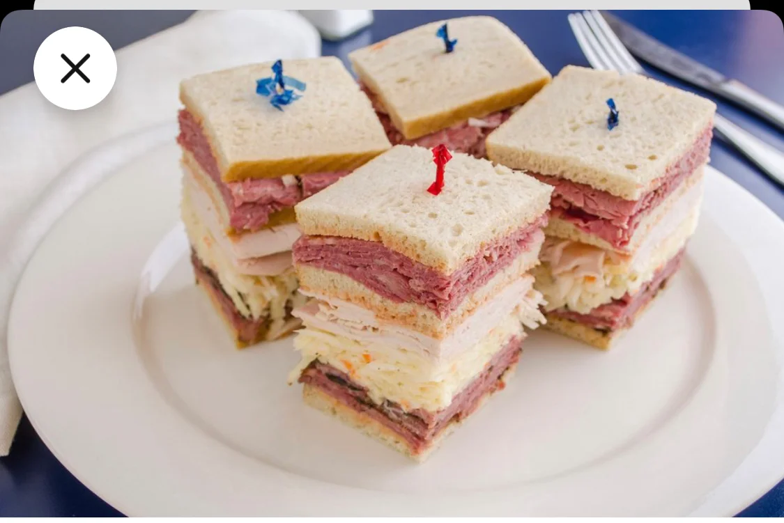 An assortment of dishes including sliced meat, salad, desserts, and sides arranged on white plates.