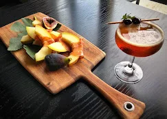 A wooden board displaying a colorful assortment of fresh fruits alongside a cocktail in a glass.