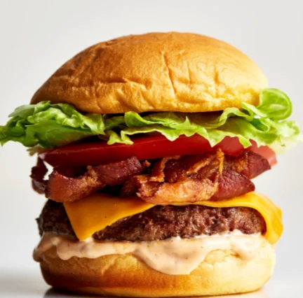 A hearty hamburger stacked with lettuce, tomato, bacon, and cheddar cheese on a golden bun.
