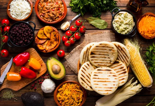 A variety of fresh ingredients and grilled arepas on a wooden table.
