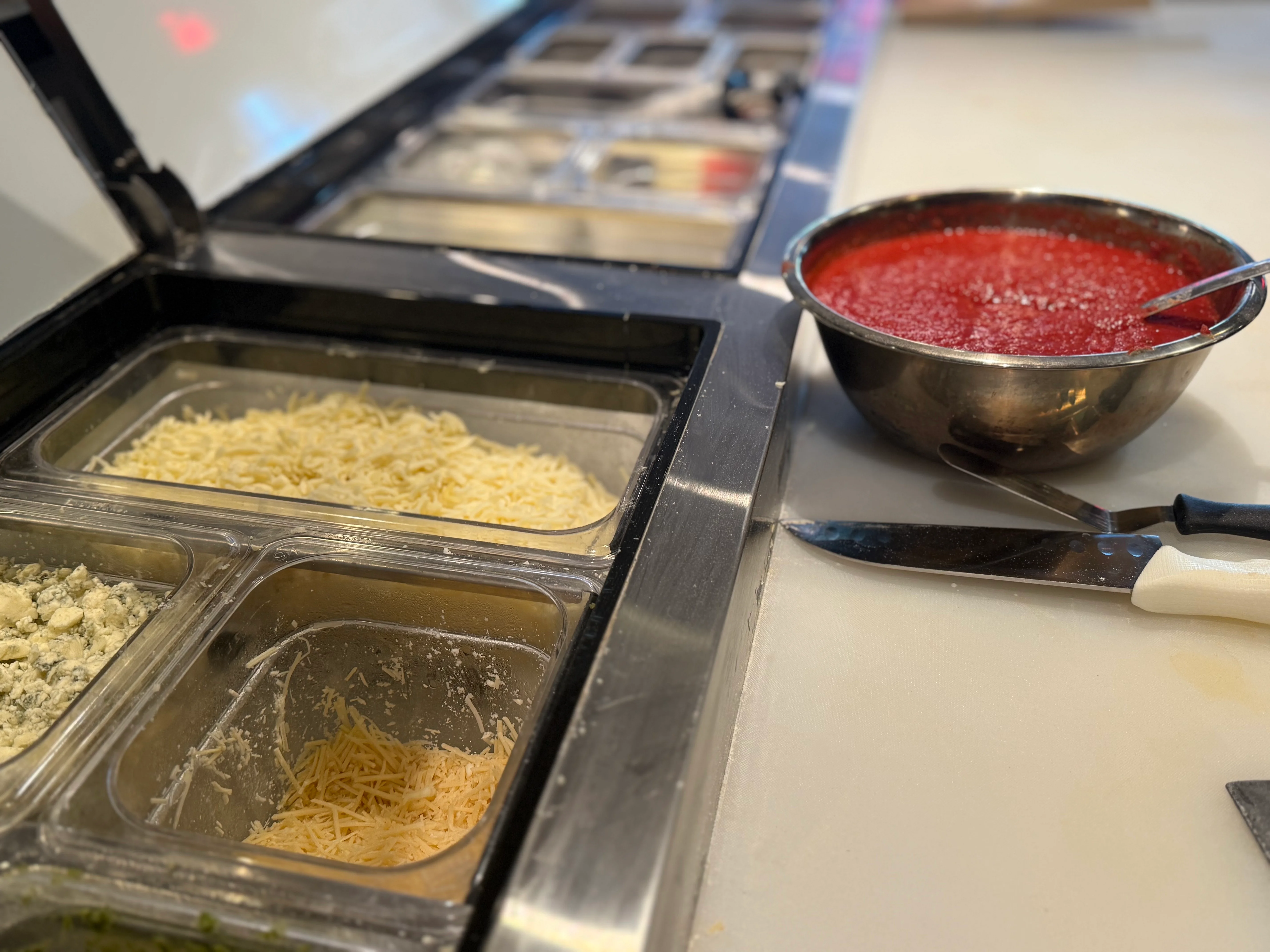 Pizza preparation station with fresh tomato sauce and cheese