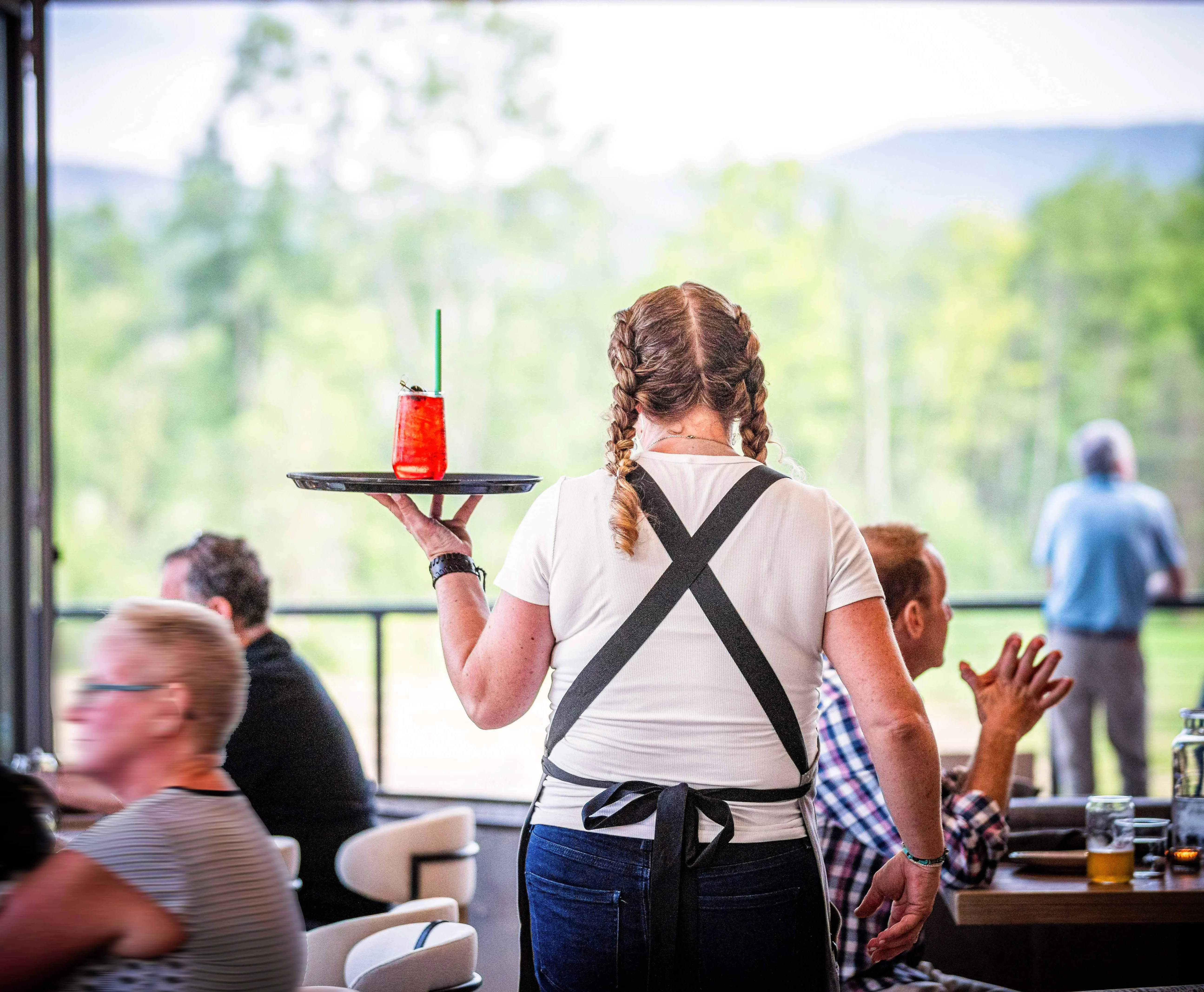 Server carrying a vibrant cocktail on a tray in a restaurant setting