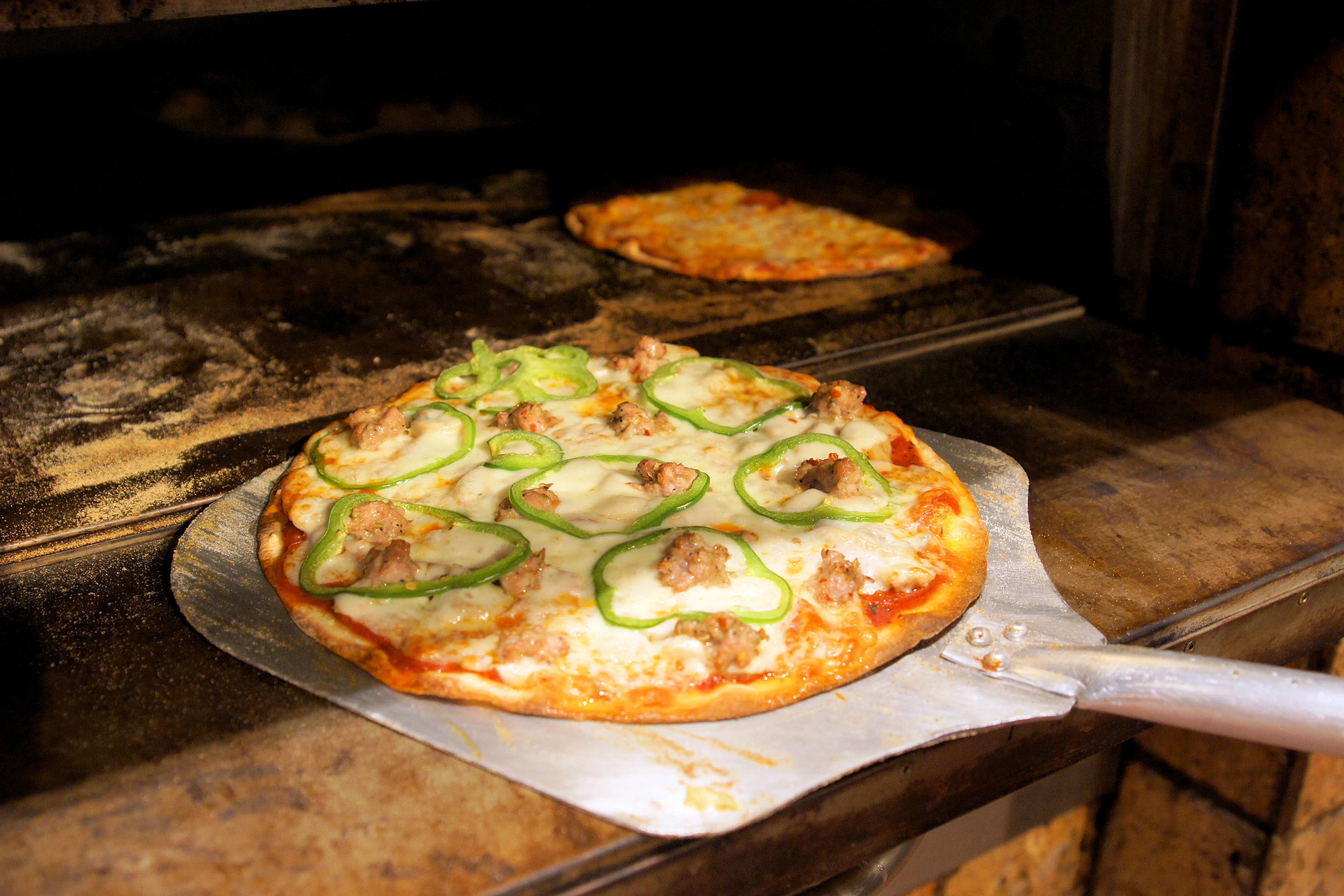 Freshly baked sausage and green pepper pizza from a wood-fired oven
