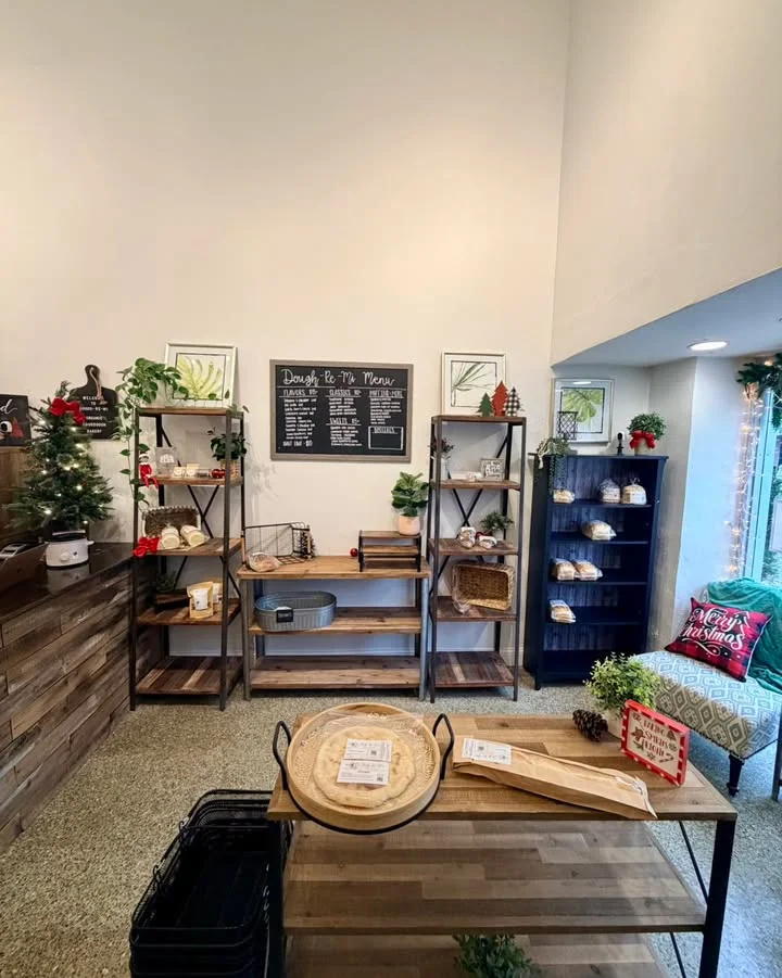 A cozy display area with various shelves showcasing baking products and decorative items. The menu is visible on a chalkboard, and festive decor adds a seasonal touch.