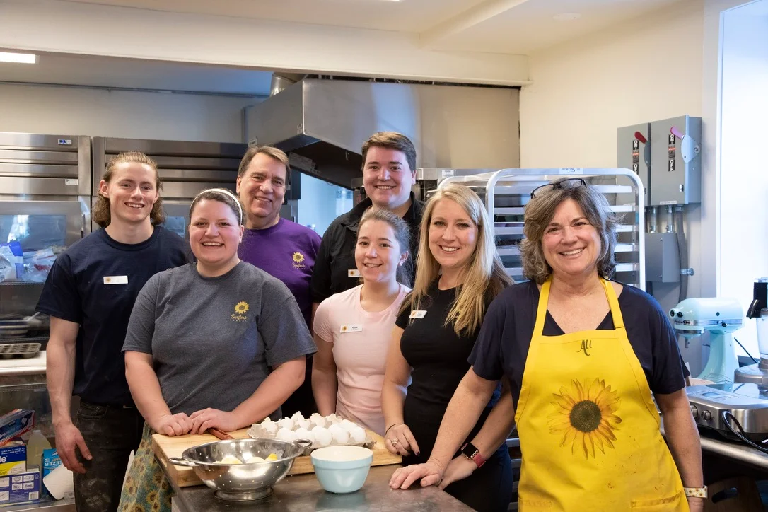 Group of staff members smiling in a kitchen setting with baking ingredients.