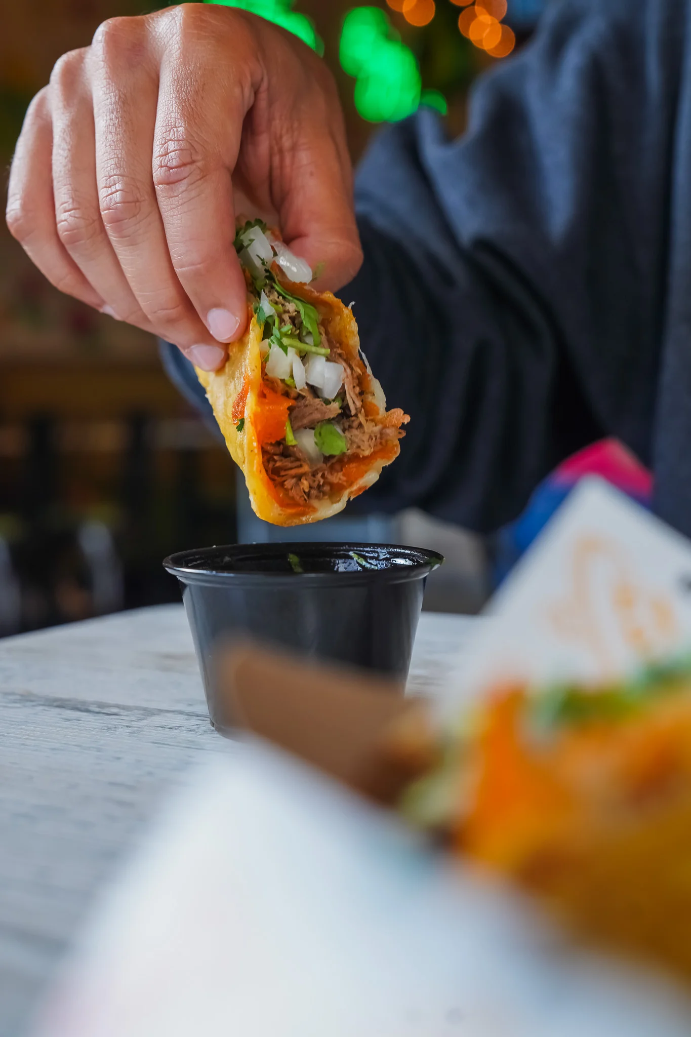 Hand holding a taco with pulled pork and toppings for dipping