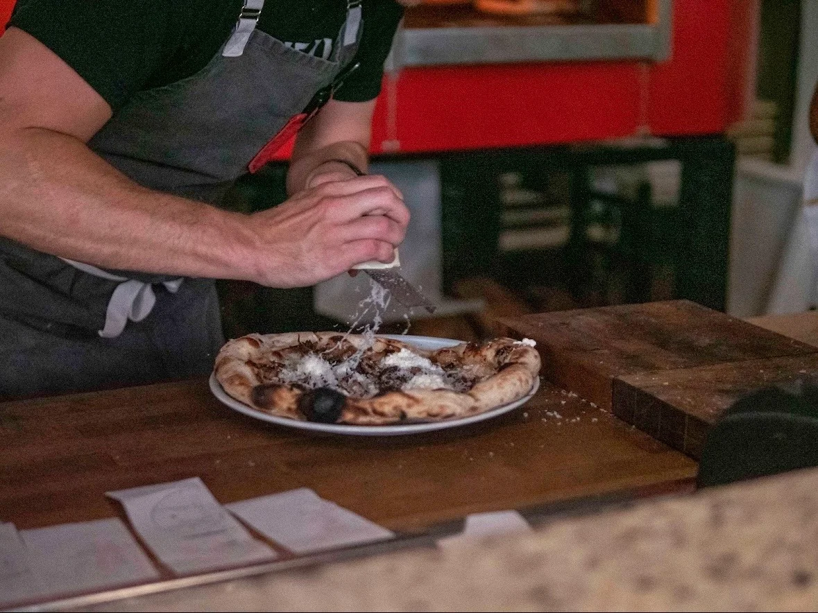 Chef finishing a Neapolitan pizza with cheese