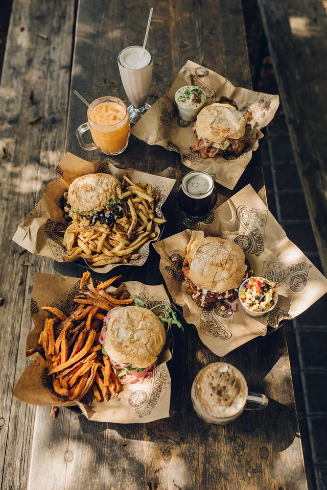 Assorted gourmet burgers with fries and milkshakes on a rustic wooden table