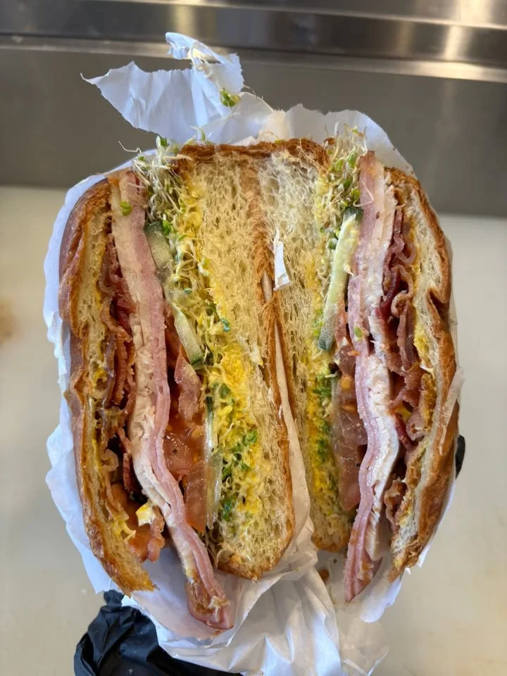 A cross-section of a sandwich filled with meats, lettuce, and other fresh ingredients, served on toasted bread.