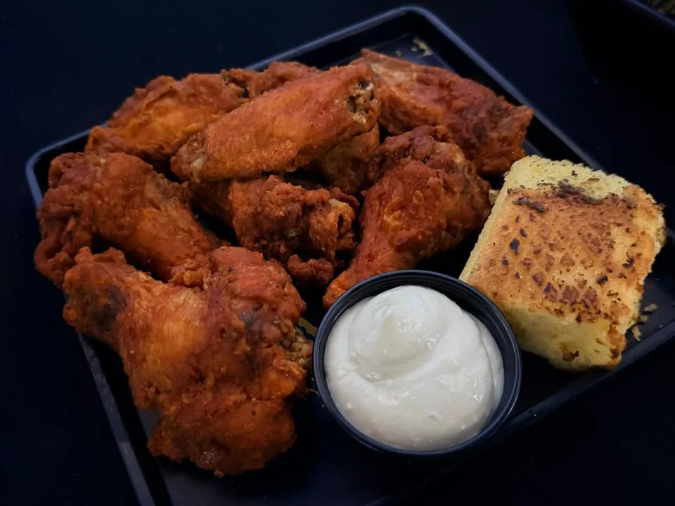 A plate of crispy fried chicken wings alongside a portion of cornbread and a creamy dipping sauce.