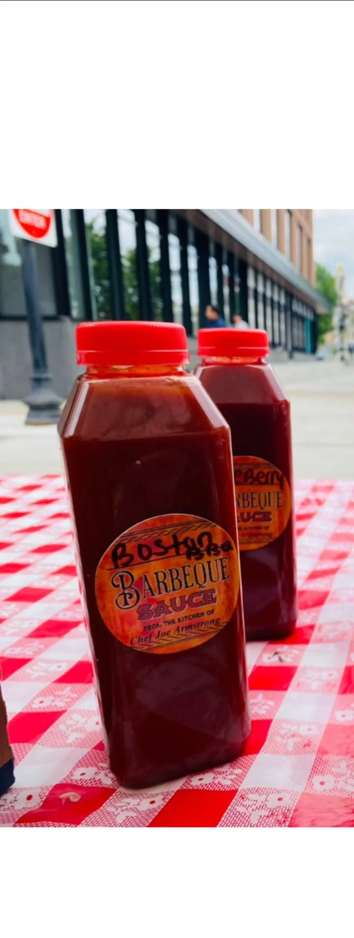 Bottles of barbecue sauce with a bright red cap displayed on a checkerboard tablecloth.