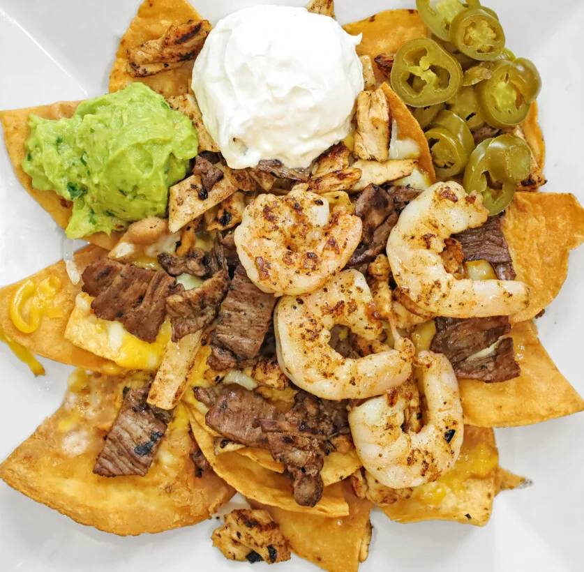 Loaded nachos with shrimp and steak, topped with guacamole and sour cream