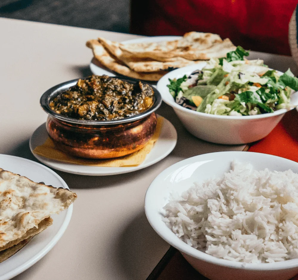 Indian meal with white rice, a bowl of brown curry, salad, and naan bread.