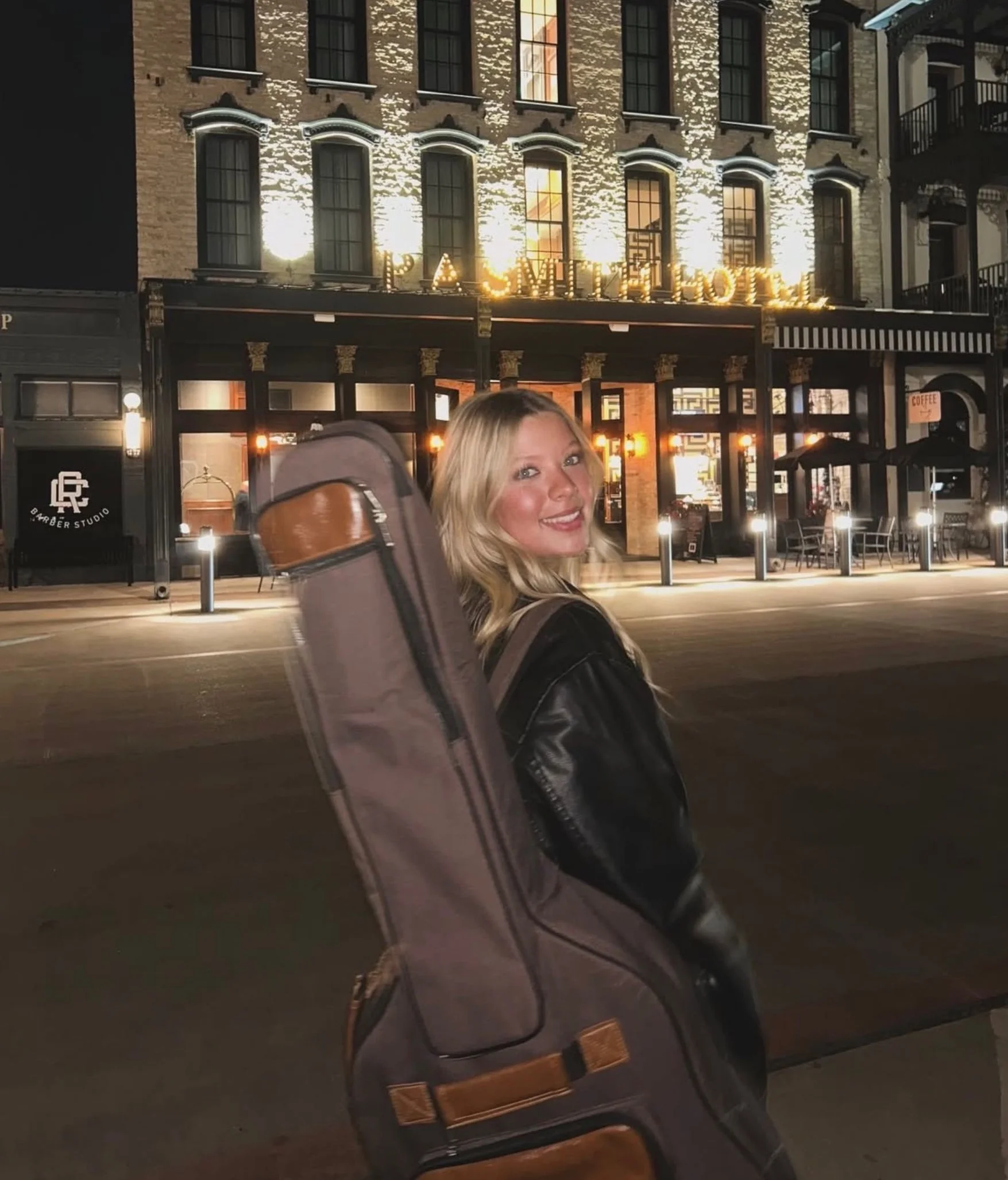 Woman with guitar case outside a historic hotel at night