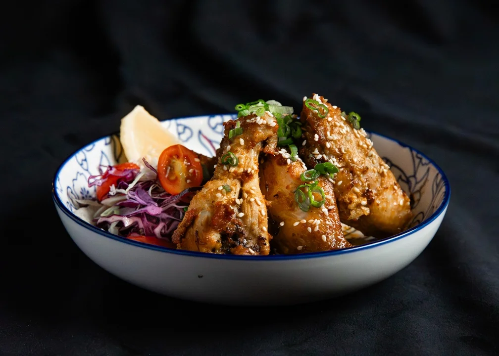 A dish featuring fried chicken wings topped with green onions and sesame seeds, served with a side salad.