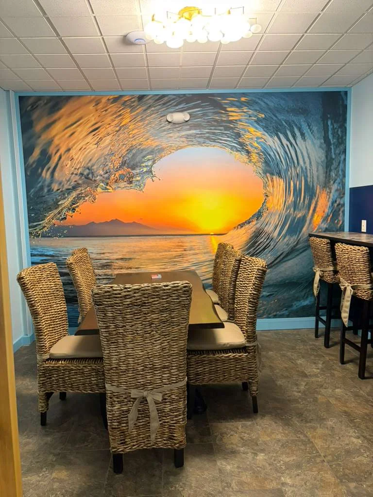 A spacious dining area with woven seating and tables, adorned with hanging plants and decorative boats.