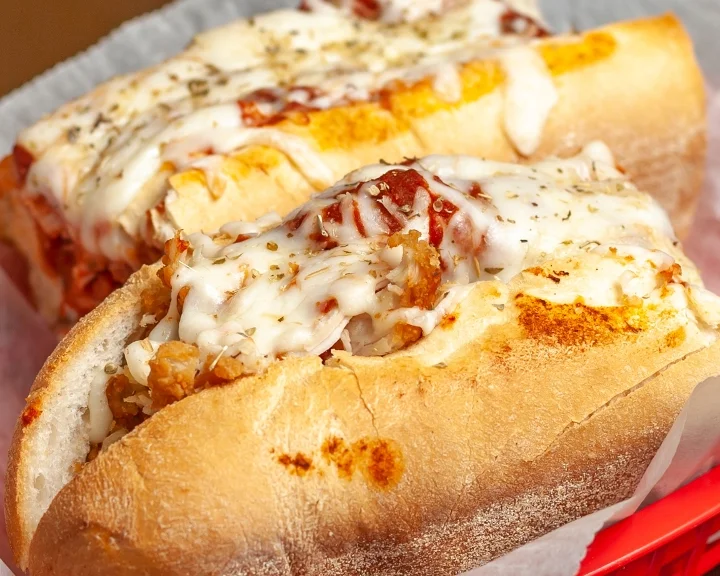 Two cheesy sandwiches filled with meat and marinara sauce, served in a red basket lined with parchment paper.