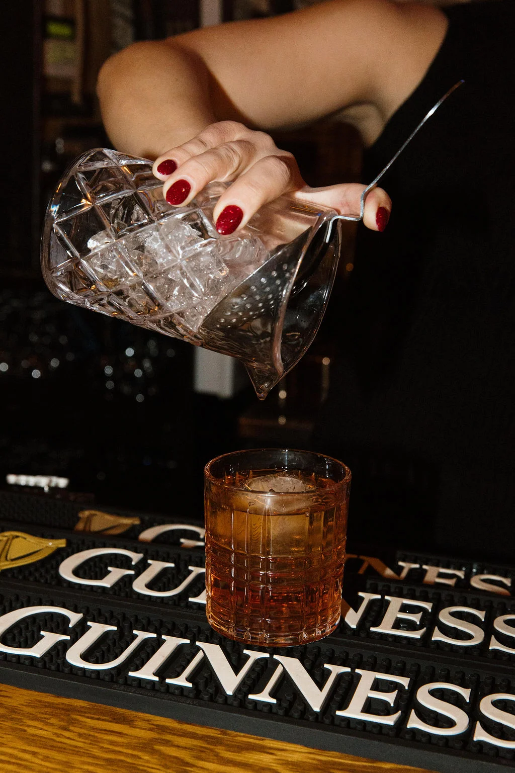 Bartender pouring ice into a cocktail glass at a bar