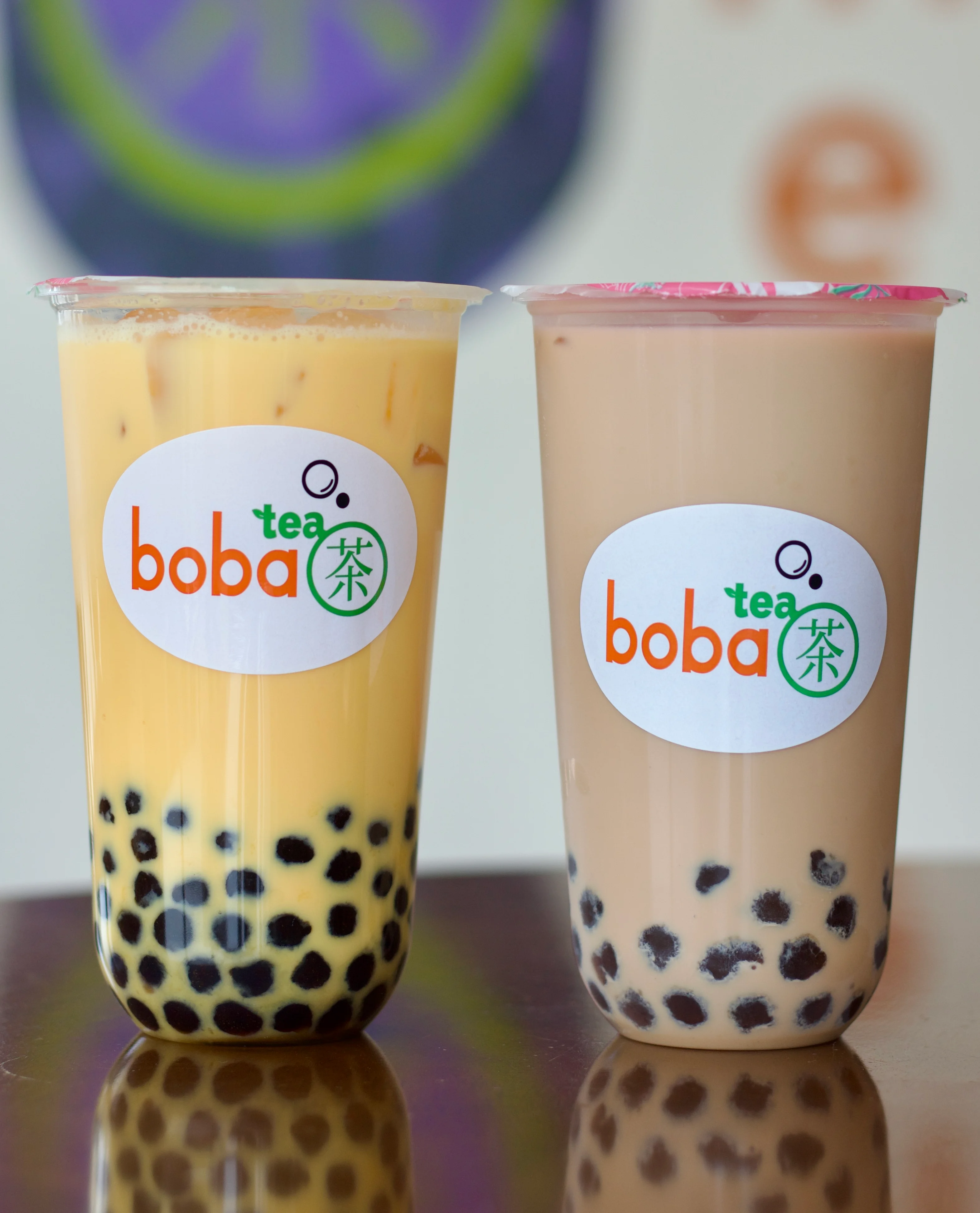 A hand holding a cup of boba tea with a purple straw. The cup features a label with the brand name and a decorative background.