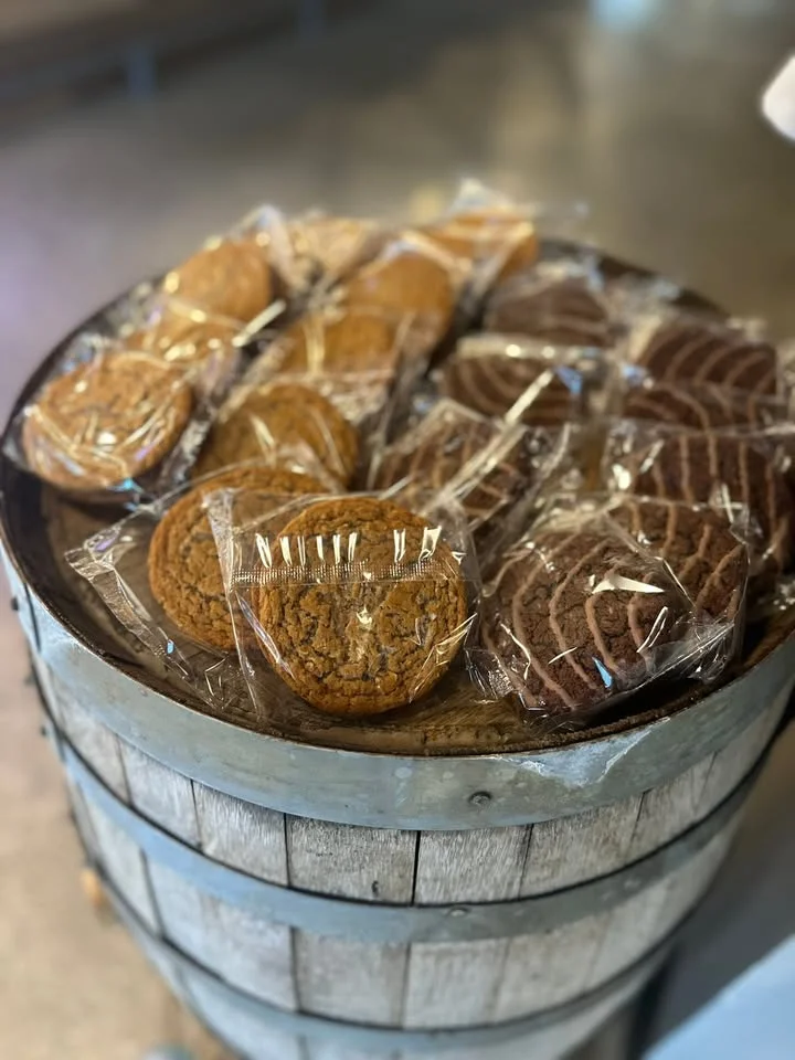 A wooden barrel filled with various cookies, each individually wrapped. The cookies come in different colors and sizes, displayed in a casual setting.