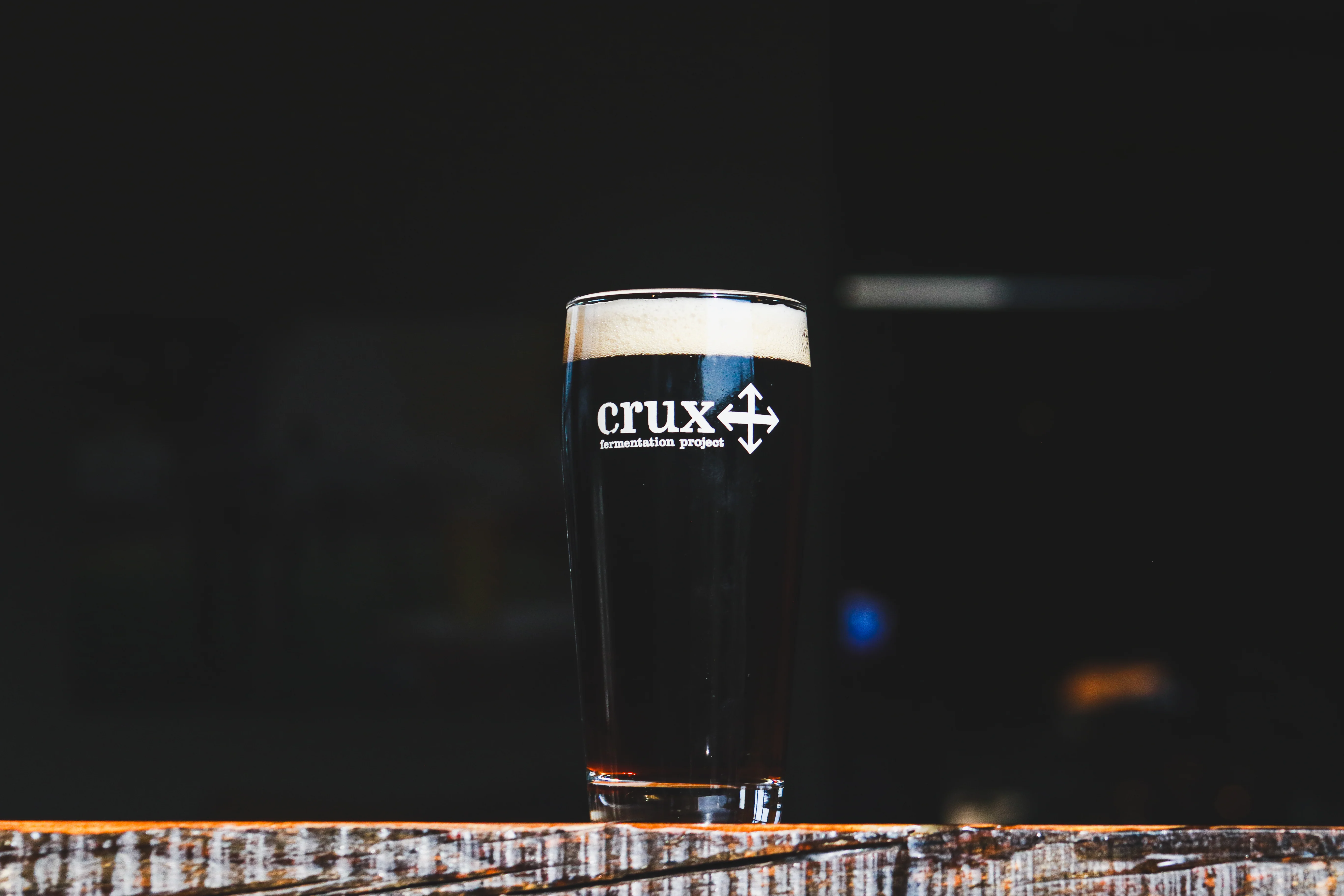 A glass of dark lager beer on a wooden table with a blurred background.