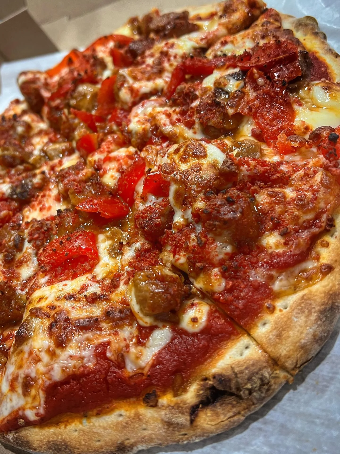 A pizza topped with various ingredients, including red peppers and sausage, showing a crispy crust and melted cheese.