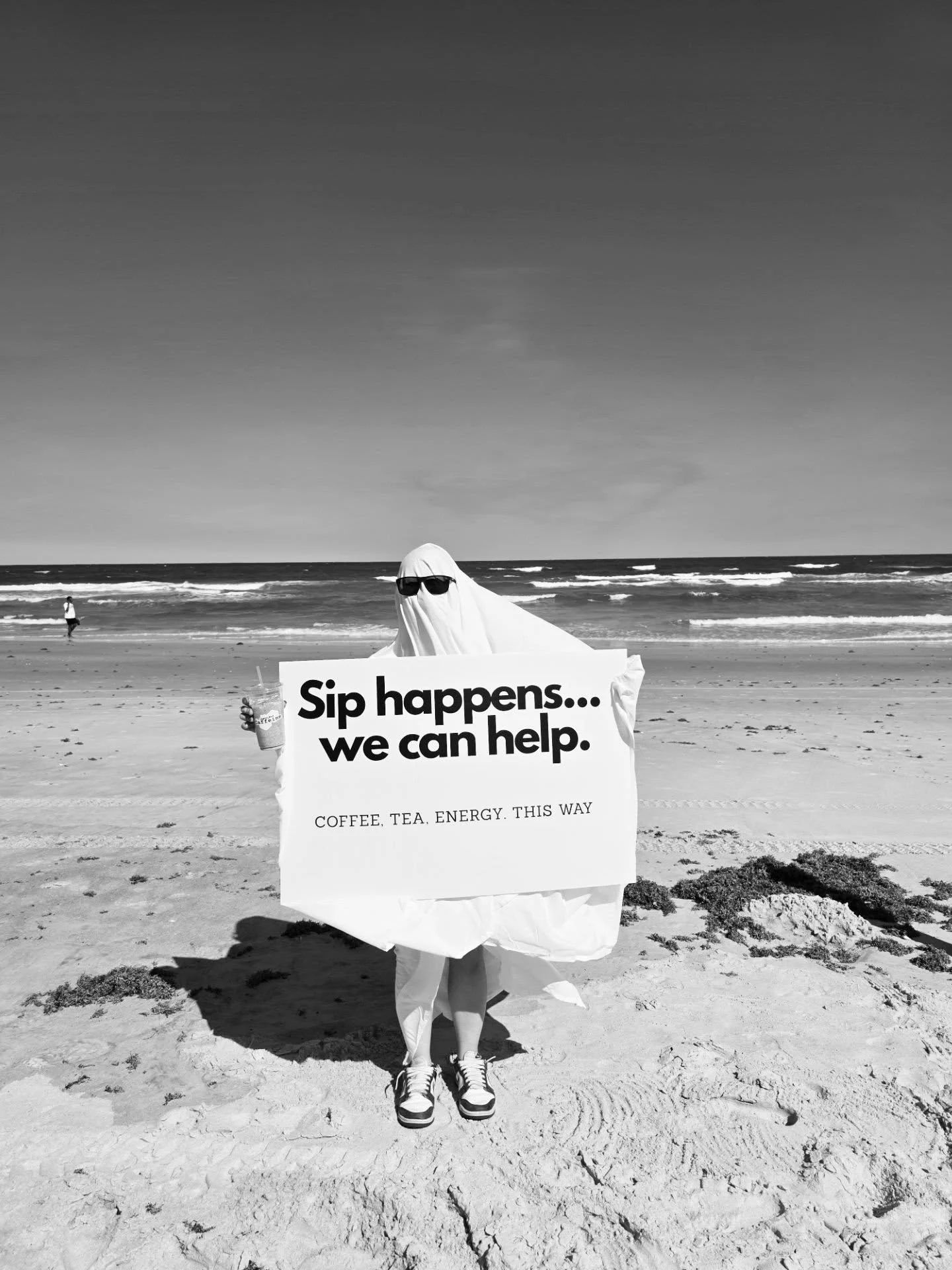 Person in a ghost costume holding a humorous sign on the beach