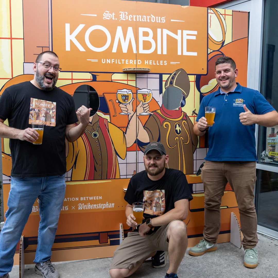 Three friends enjoying St. Bernardus Kombine beer at a vibrant event backdrop.
