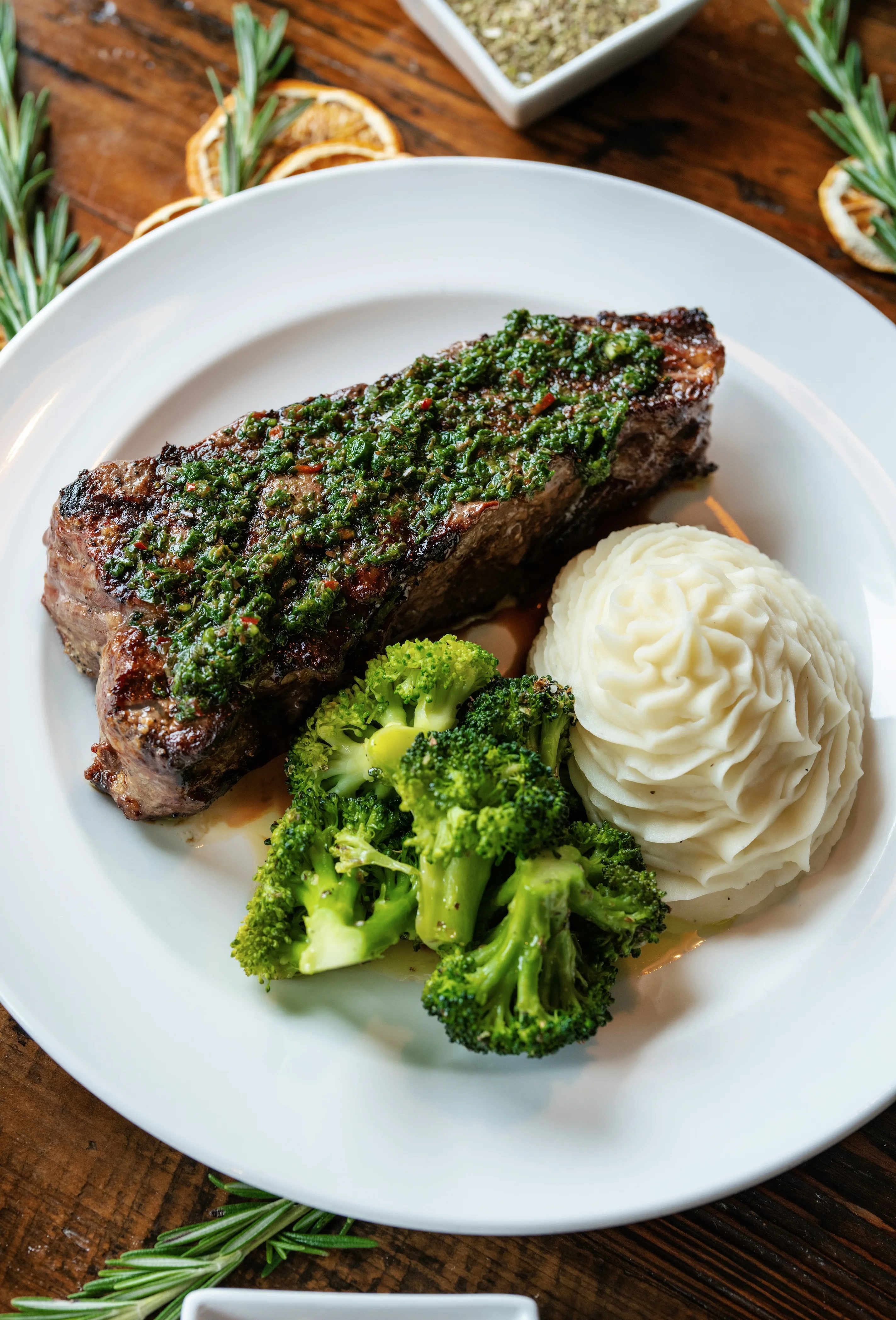 Grilled steak with chimichurri sauce and sides of broccoli and mashed potatoes