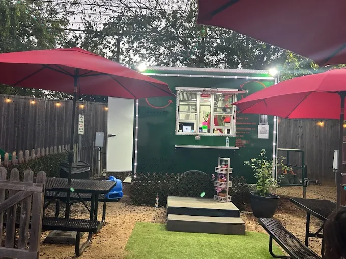 Outdoor food truck dining area with red umbrellas and picnic tables