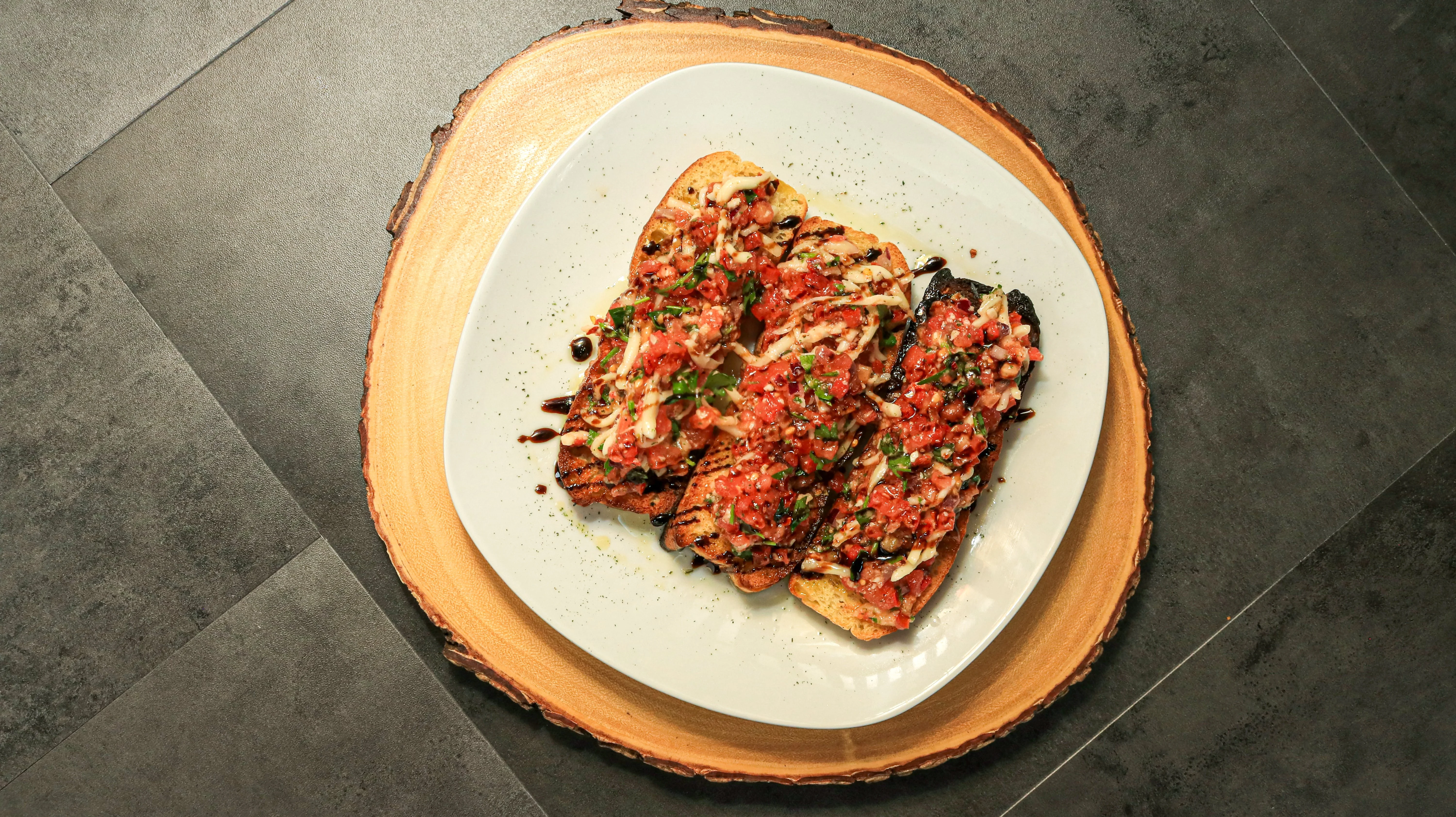 Grilled bread slices topped with a mixture of diced tomatoes, herbs, and drizzled with a balsamic reduction. The dish is presented on a wooden serving platter.