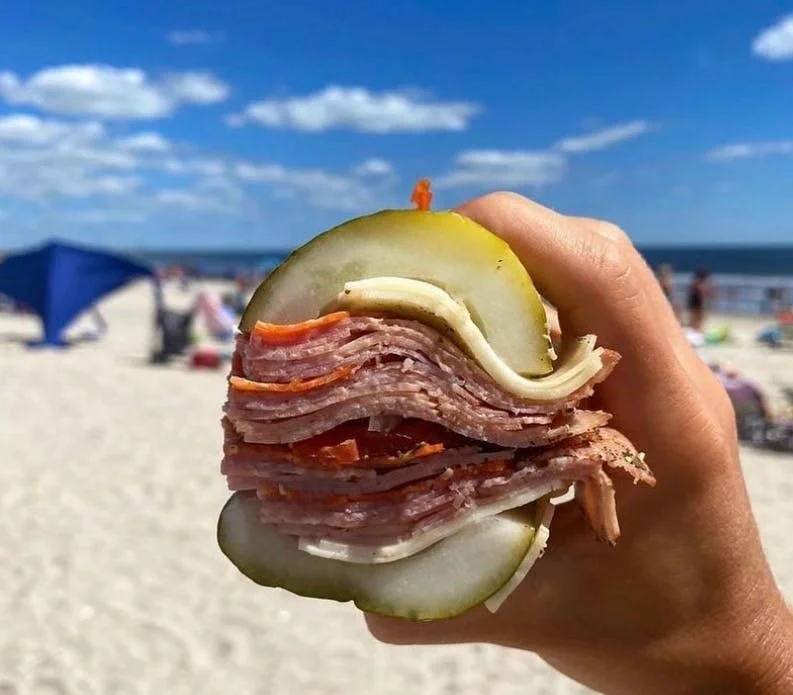 Layered deli meat sandwich with pickles at the beach