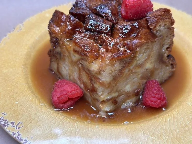 A delicious bread pudding topped with fresh raspberries served on a decorative plate.