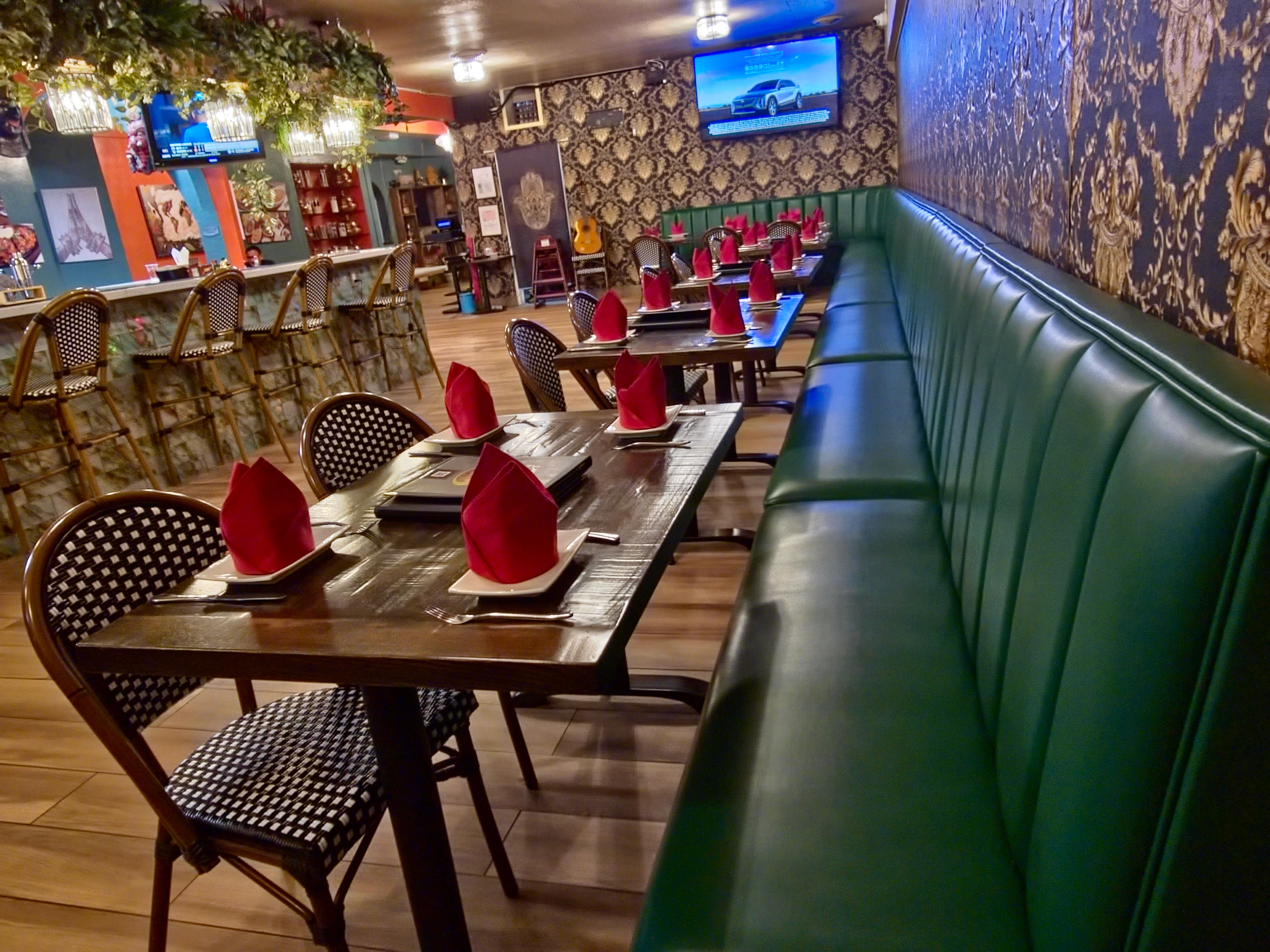 Sugandh lounge with green banquette seating, wooden tables, and red napkins beside the bar