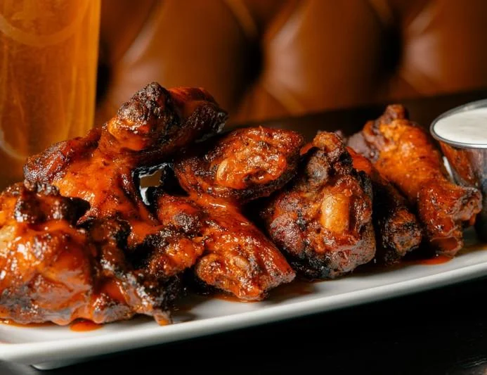 A large serving of sauced chicken wings arranged on a white platter, accompanied by a dipping sauce.