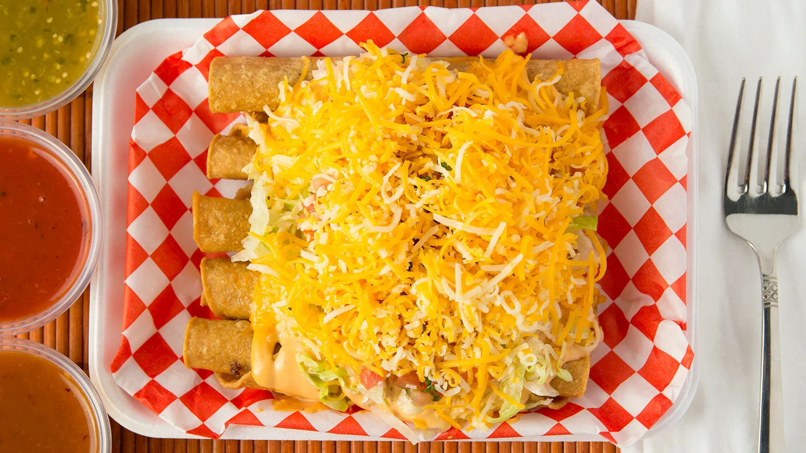 Plate of crispy taquitos topped with cheese and lettuce