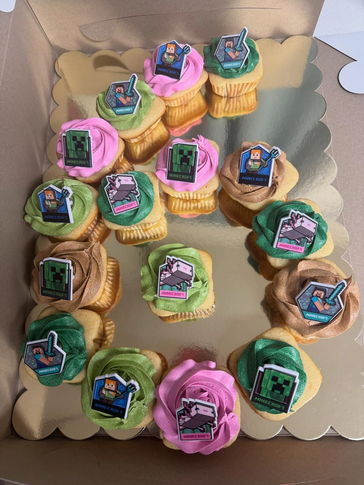 A box of colorful cupcakes decorated with themed edible images from a video game. The cupcakes feature various colors of frosting and playful designs.