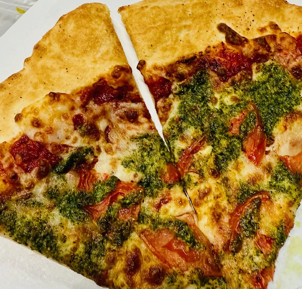Pesto pizza slice with fresh tomatoes and melted cheese