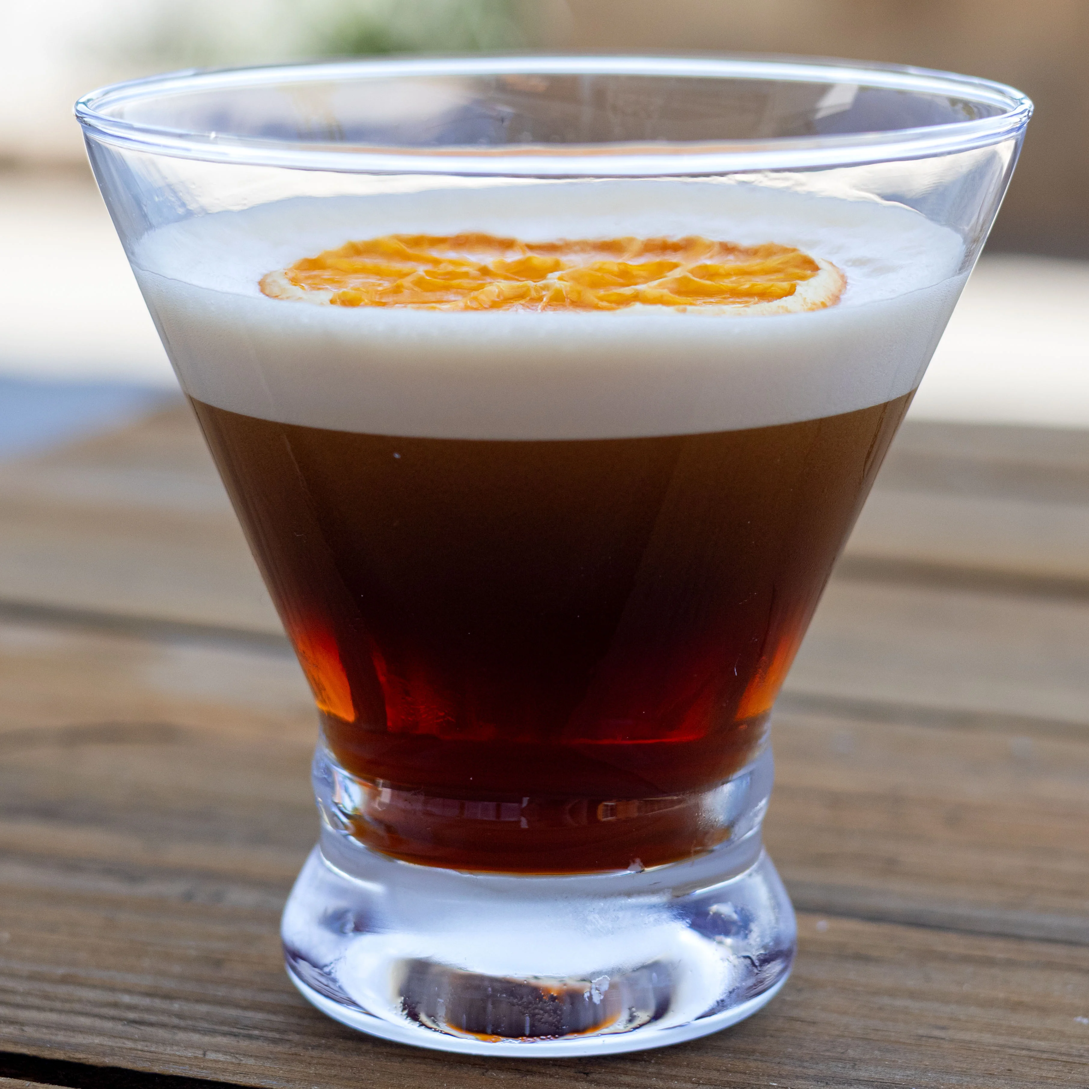 A layered cocktail with orange garnish in a clear glass.