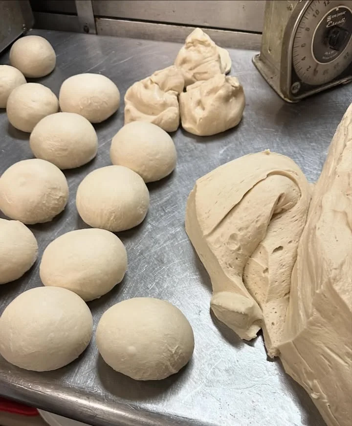 Various pieces of dough are arranged on a stainless steel surface, with some shaped as balls and others in a larger mass.