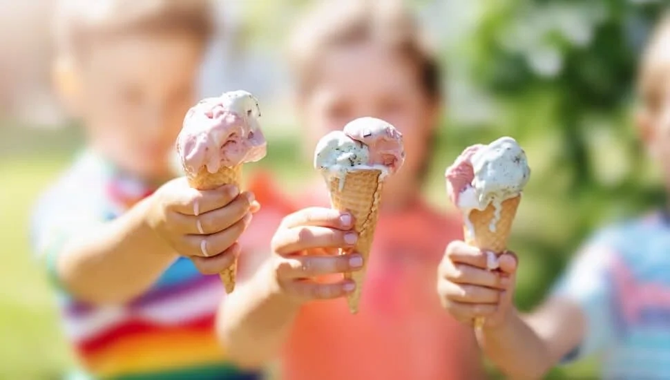 Children enjoying colorful ice cream cones in a sunny park