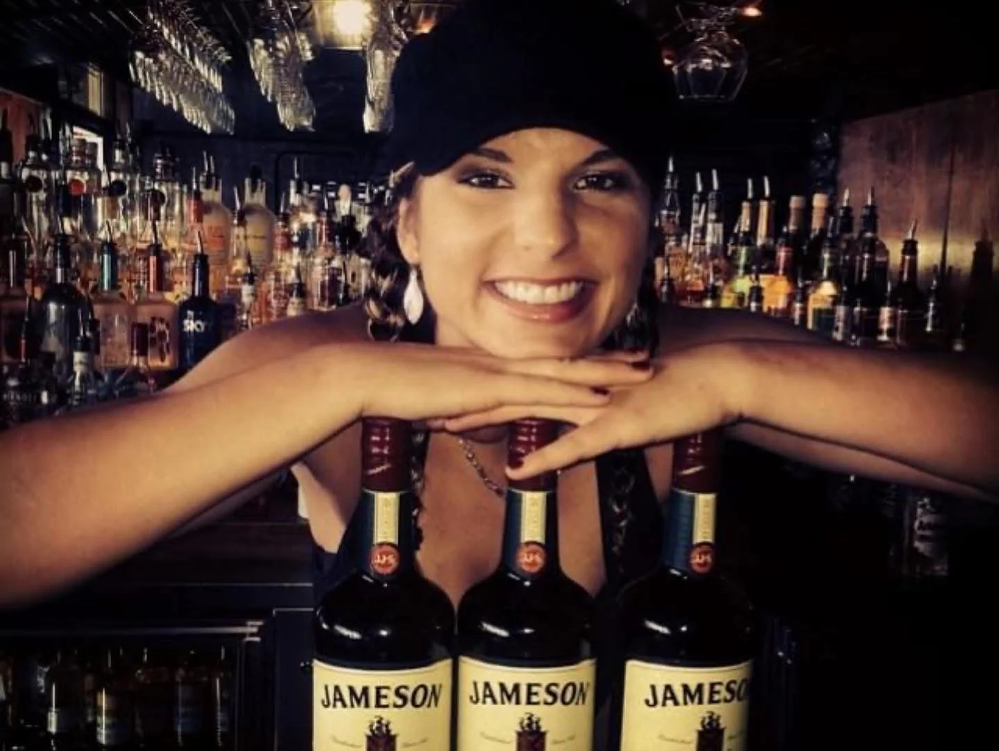 Bartender showcasing Jameson whiskey bottles at a lively bar