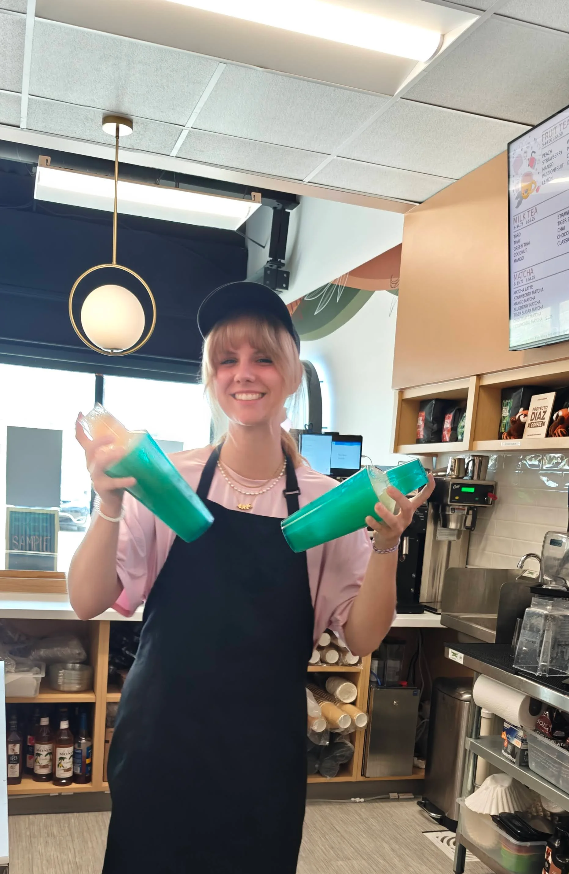 Barista smiling with colorful drink cups in a modern café