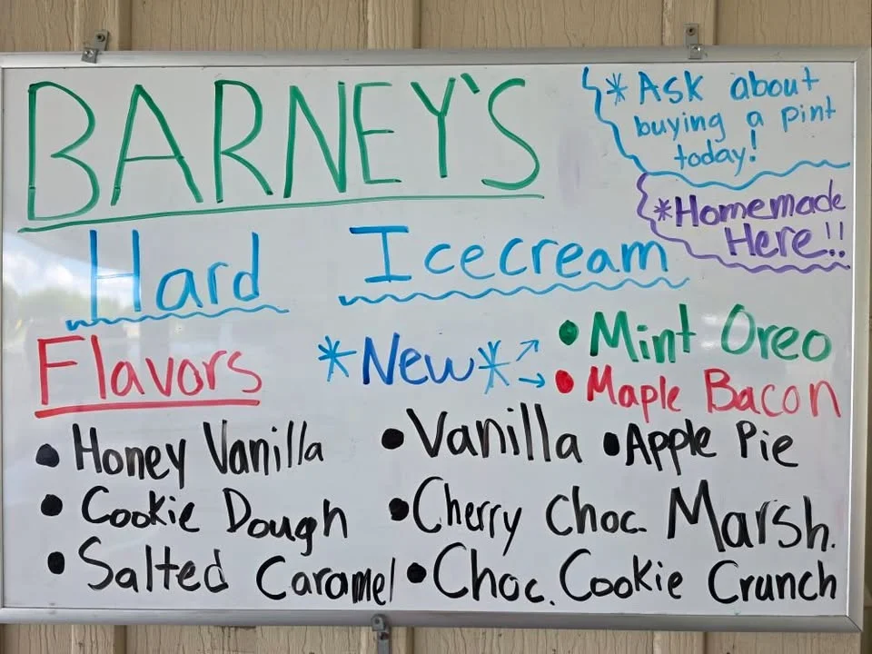 A colorful whiteboard menu showcasing various hard ice cream flavors available at Barney's, including new options like Mint Oreo and Maple Bacon.