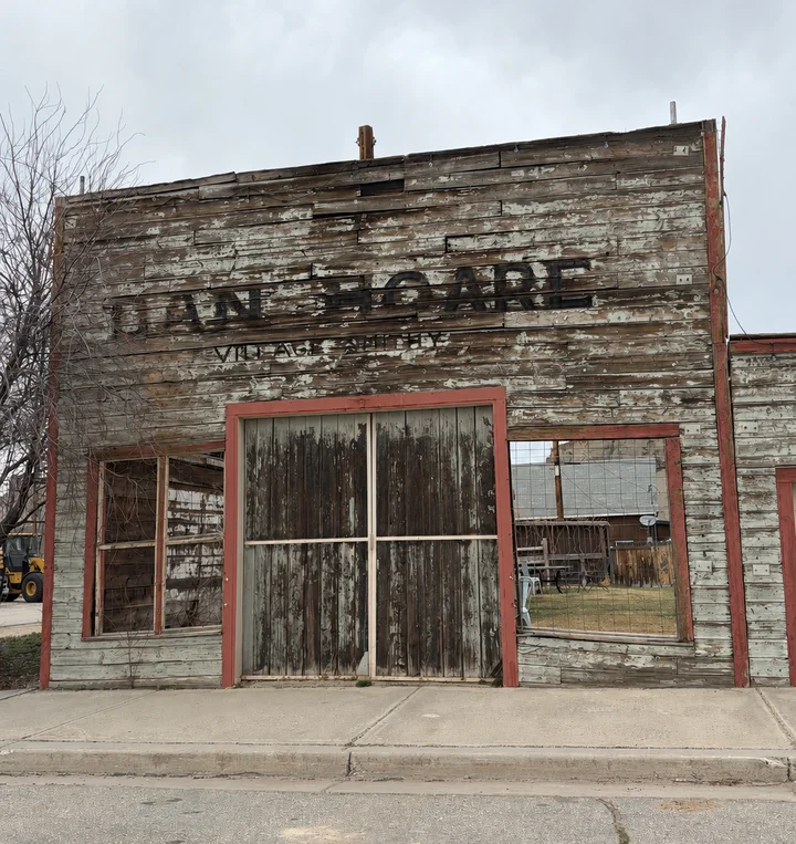 An old, weathered wooden building with a partially visible sign, featuring peeling paint and a closed entrance.
