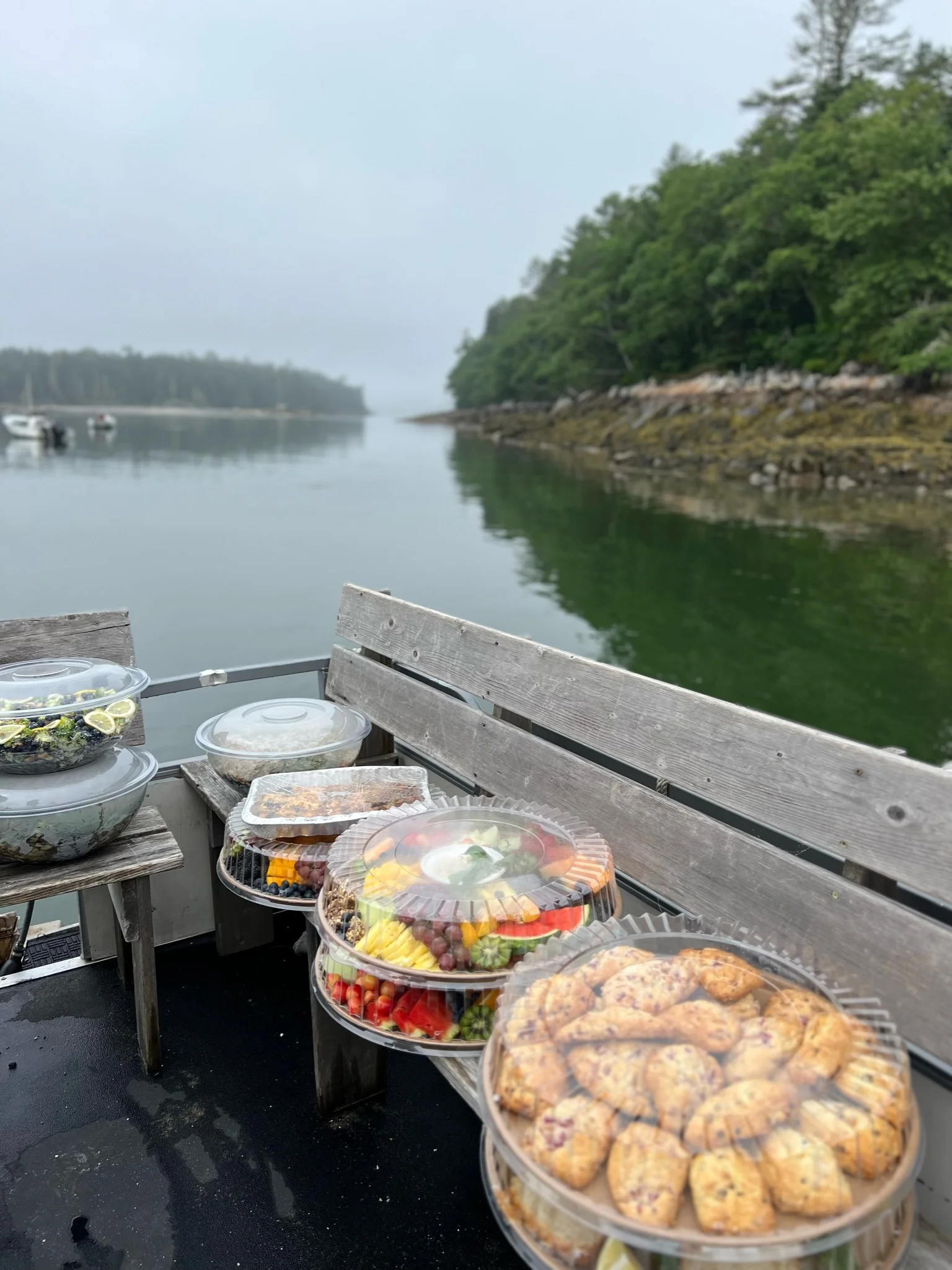 Assorted seafood and fresh fruit platters on a boat in a misty harbor