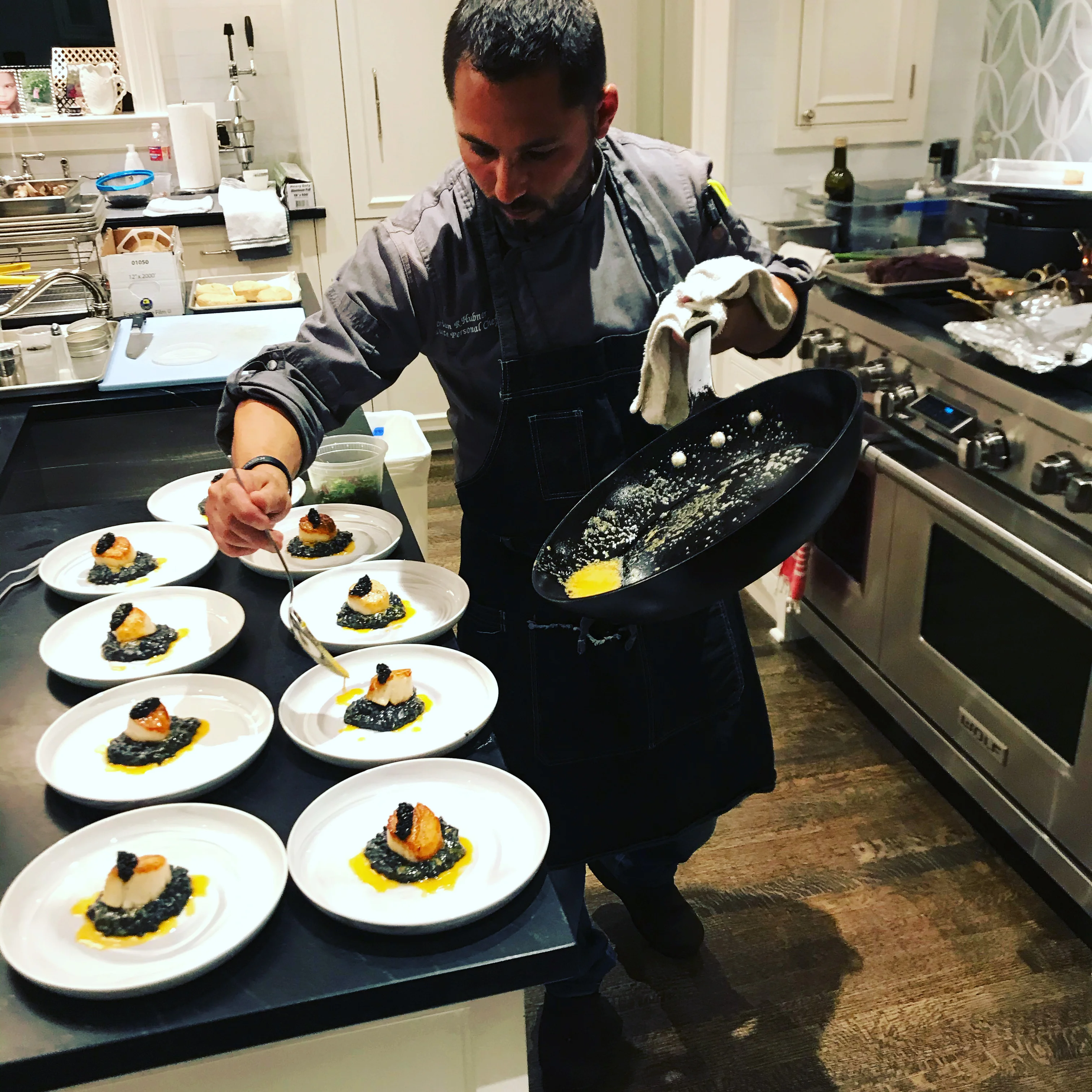 Chef plating scallops with black risotto in a modern kitchen