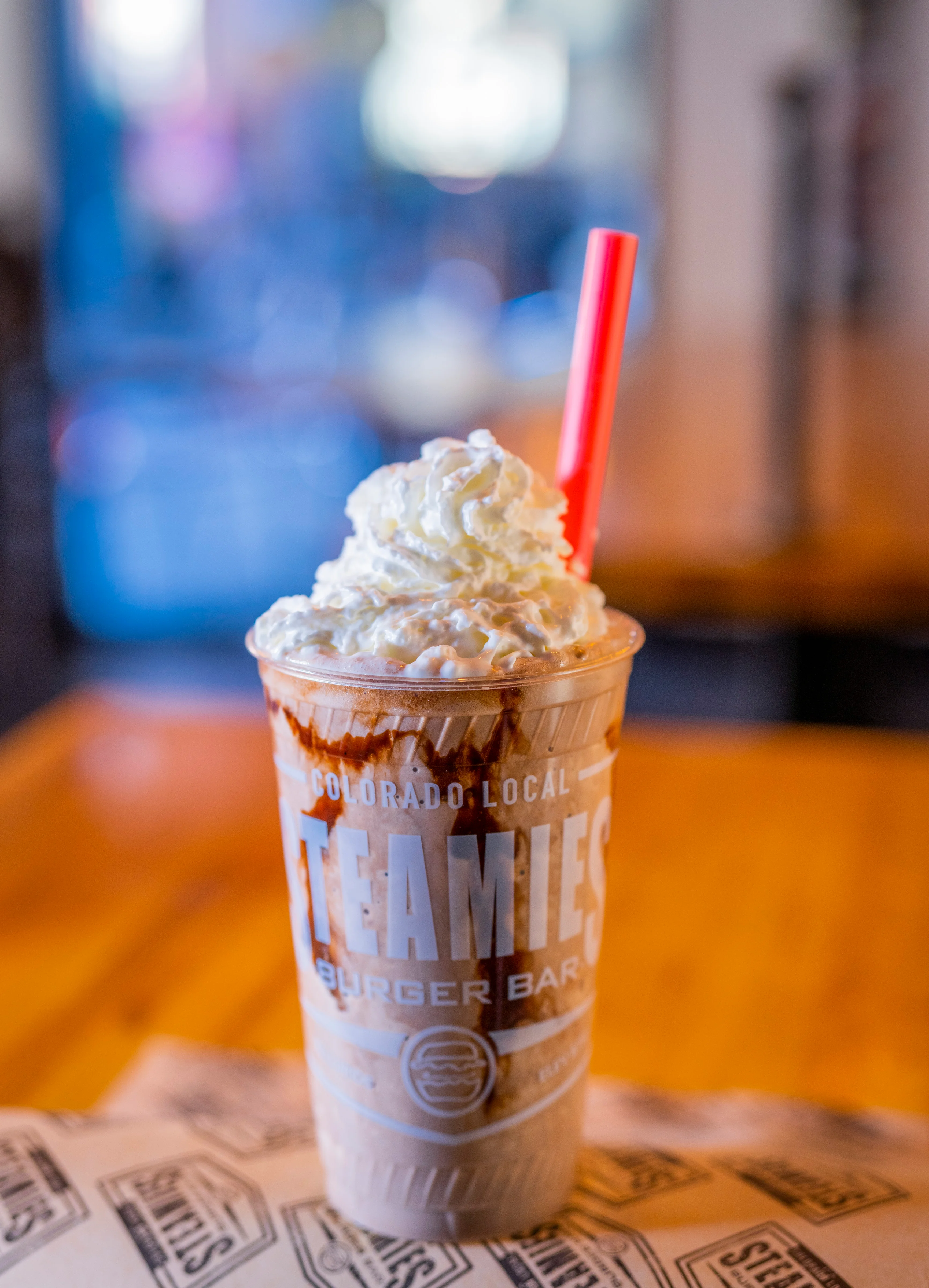 A delicious milkshake topped with whipped cream and drizzled chocolate syrup, served in a clear cup with a red straw.